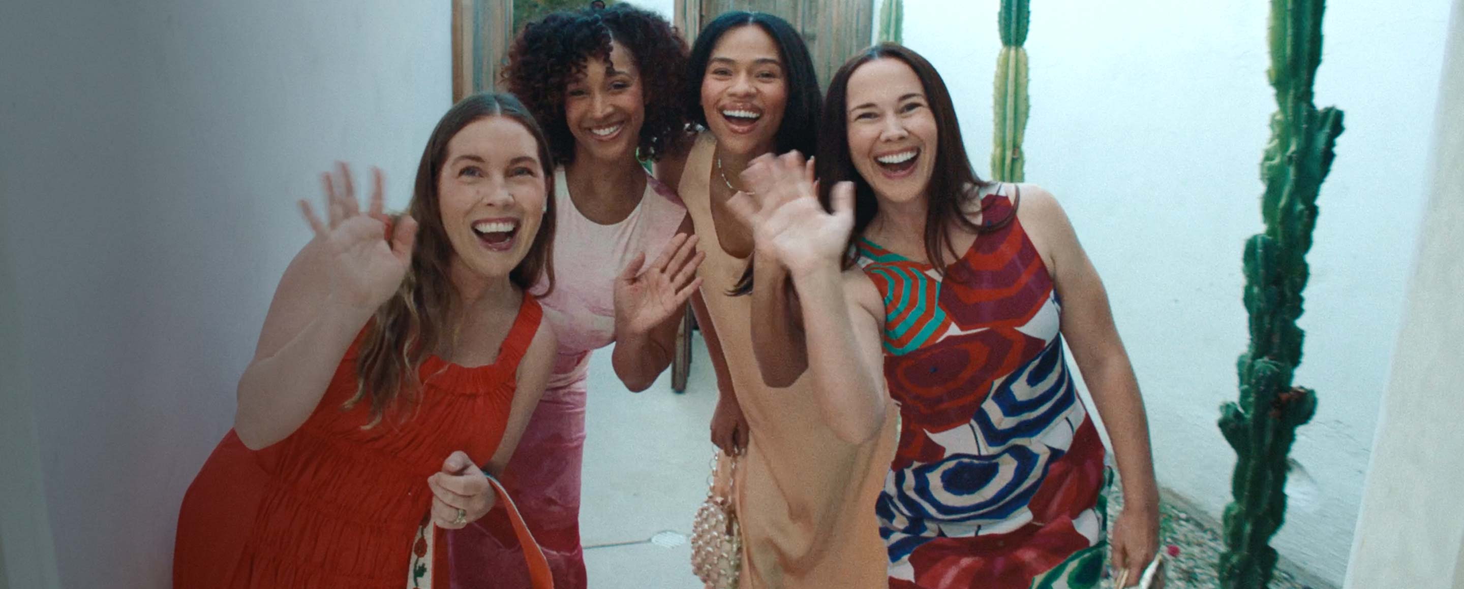 four girls smiling and waving at a camera